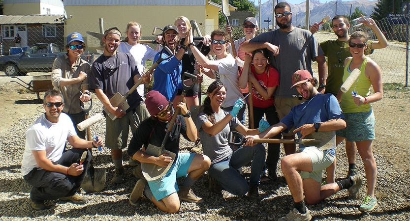 A group of people holding paint brushes pose for a group photo during a service project with outward bound.